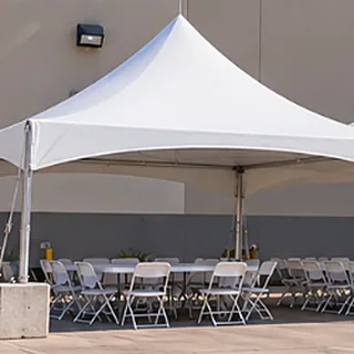 20 by 20 High Peak tent set up beside a warehouse with tables and white folding chairs